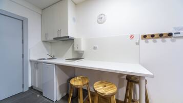A modern kitchen with white cabinets, a built-in dishwasher, a wooden bar stool, and a wall-mounted clock.