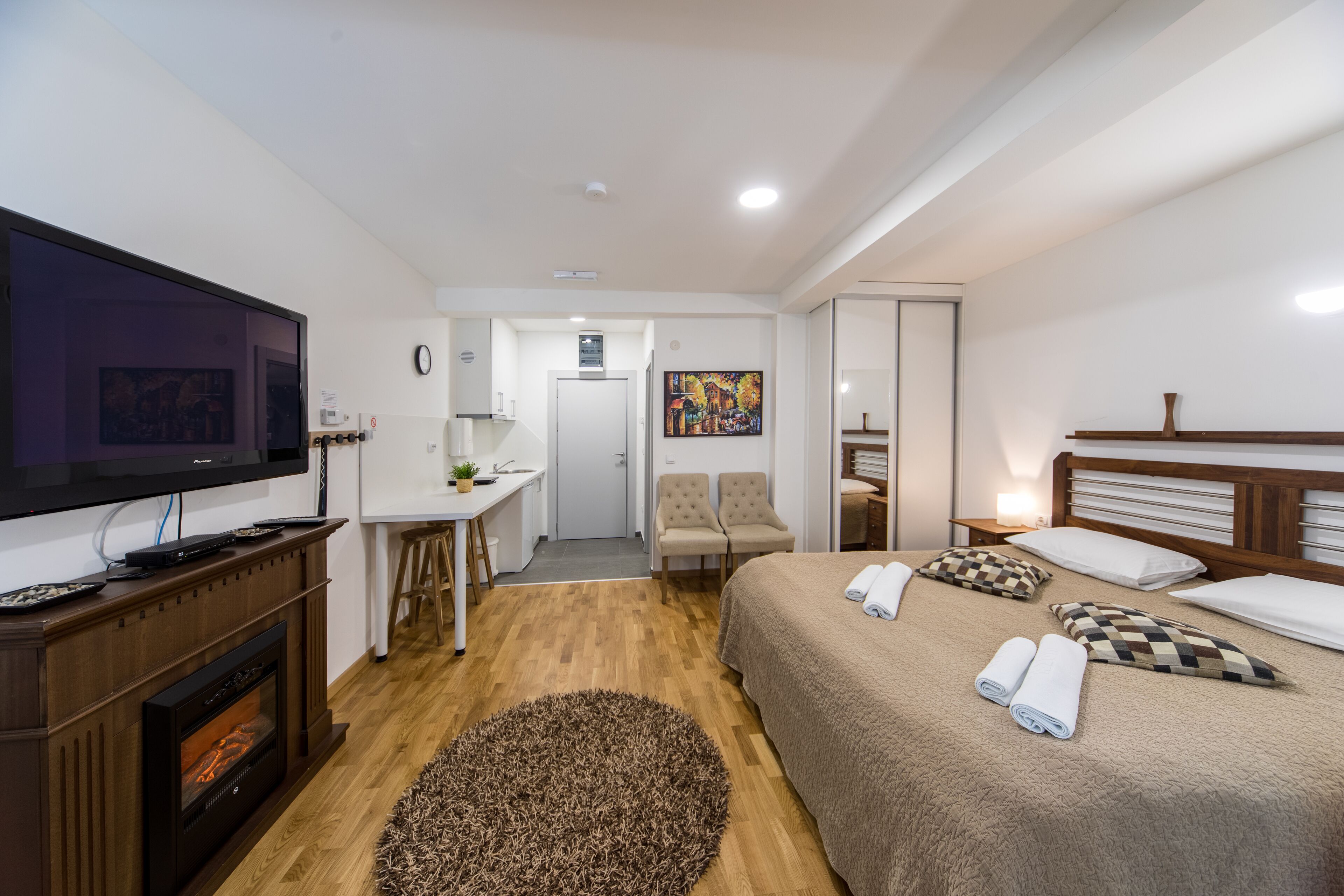 A hotel room with a bed, a TV, a desk, a chair, a fireplace, and a painting on the wall.