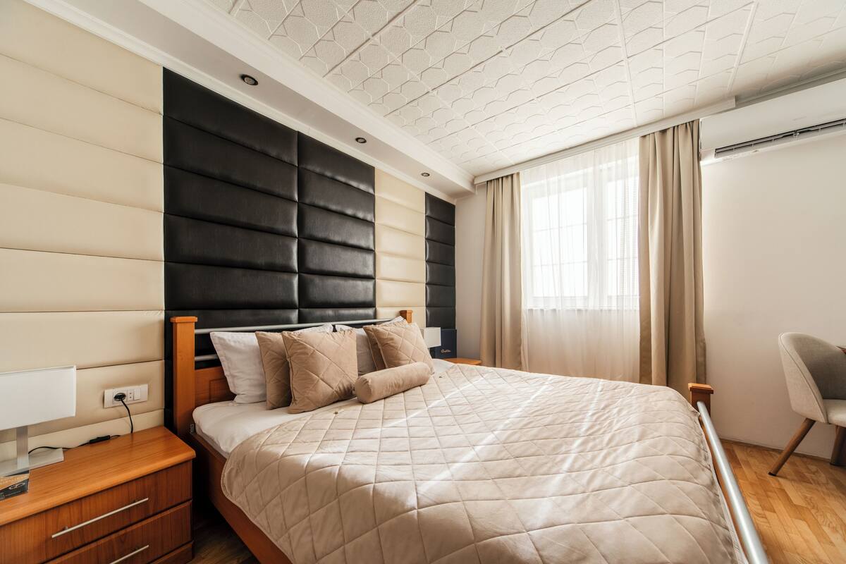 Um quarto moderno com uma cama grande, uma mesa de cabeceira, uma cadeira e uma janela com cortinas.