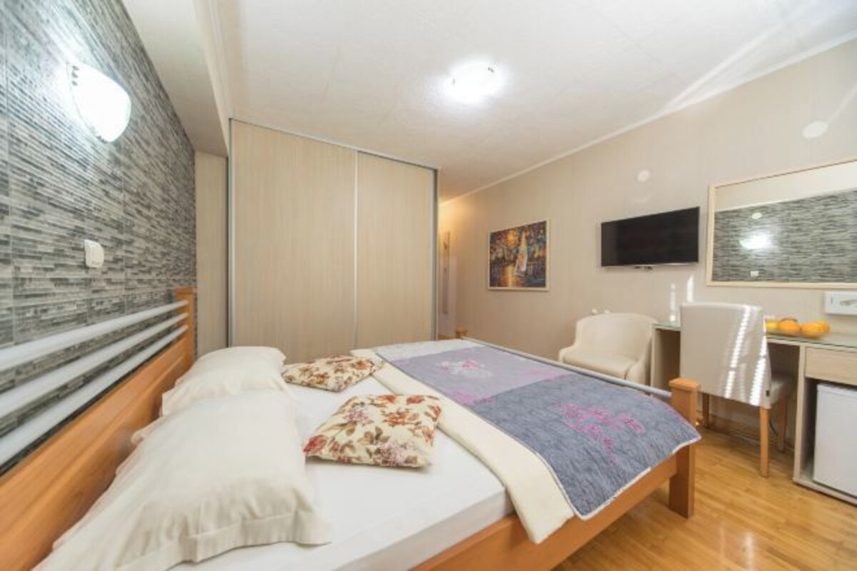 Un dormitorio con cama, escritorio, silla, televisor y un cuadro en la pared.