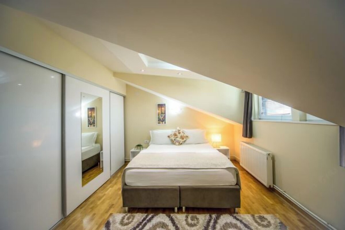 A bedroom with a bed, bedside tables, a radiator, and a window.