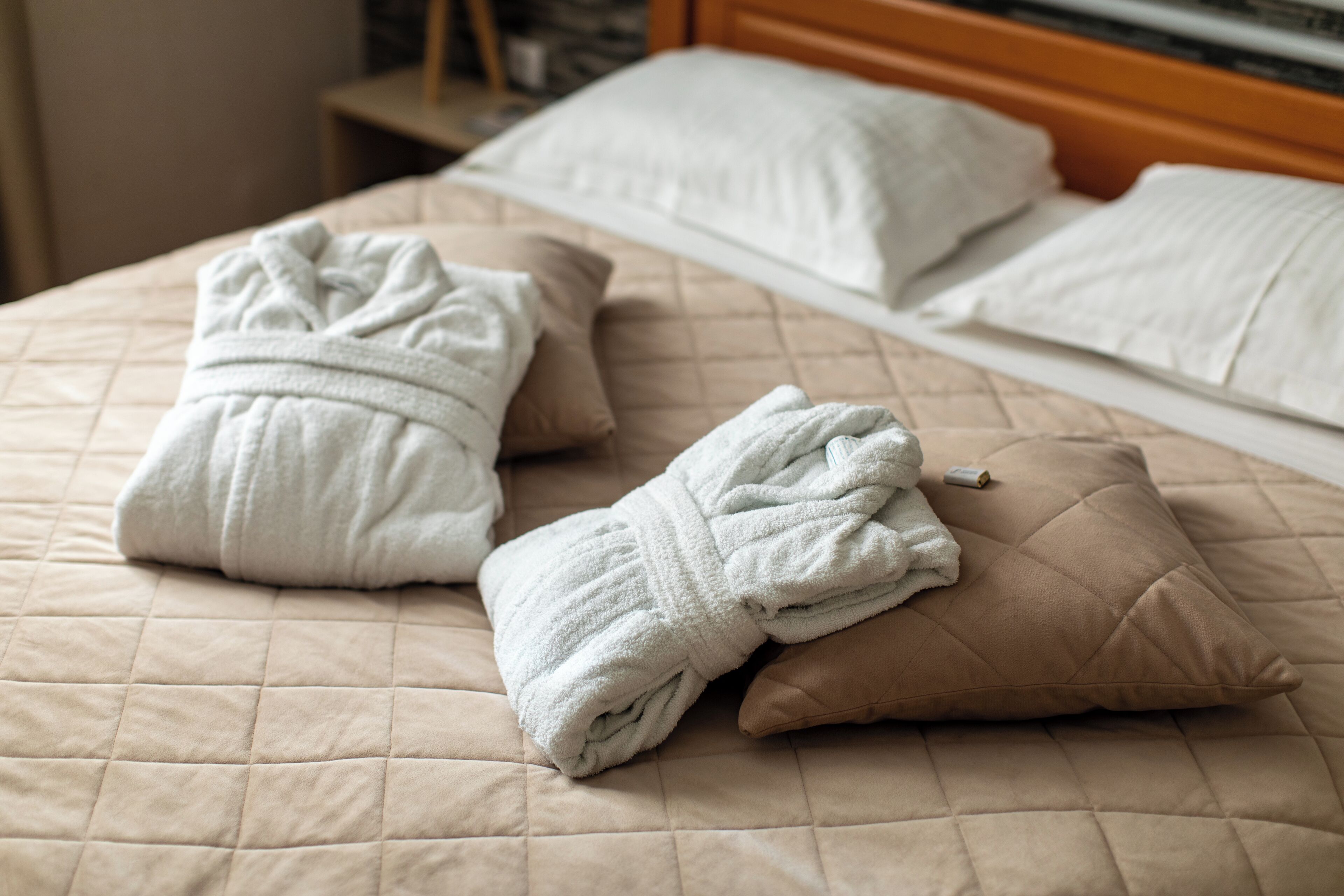 Una cama con una colcha beige acolchada, dos toallas blancas y una almohada marrón.