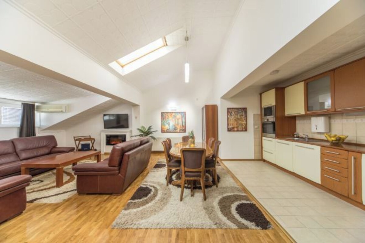 Amplia sala de estar con un conjunto de sofás, una mesa de comedor y una cocina con armarios y electrodomésticos.