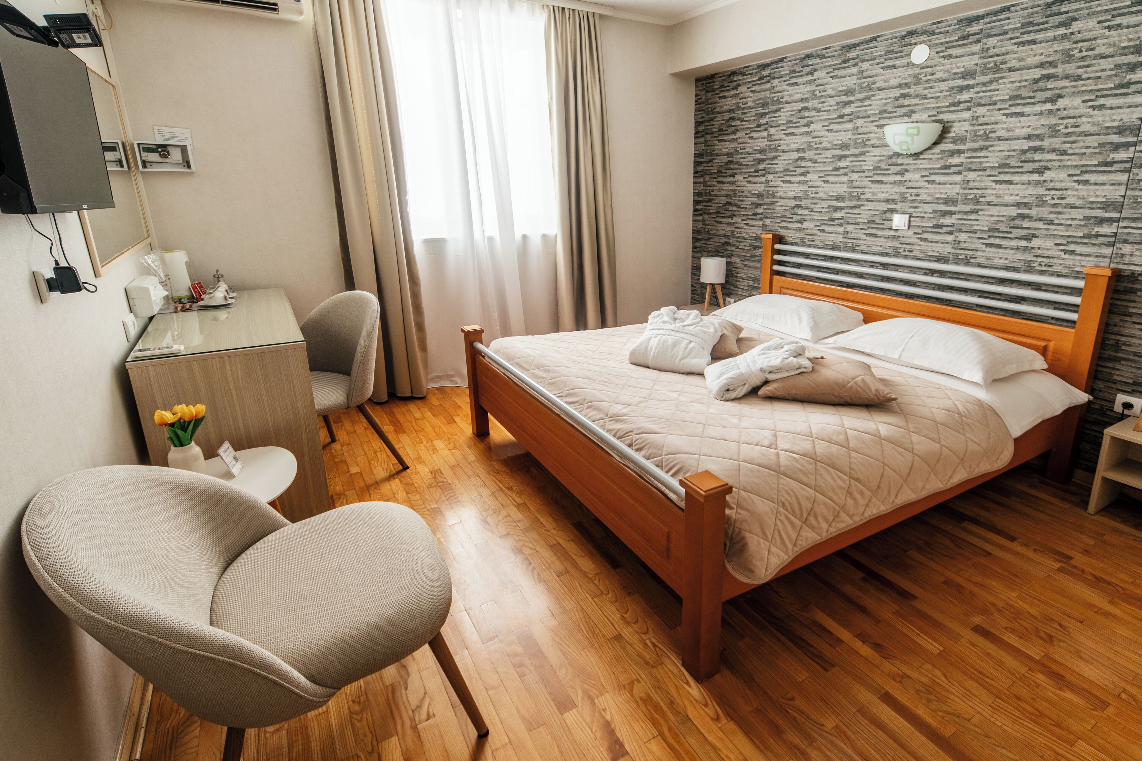 Habitación de hotel con cama de madera, un escritorio con silla, una pequeña mesa con un florero y una pared con diseño de piedra.