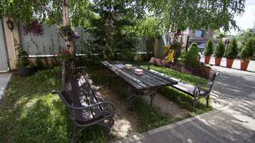 An outdoor seating area with a wooden table and benches, surrounded by potted plants and a tree.