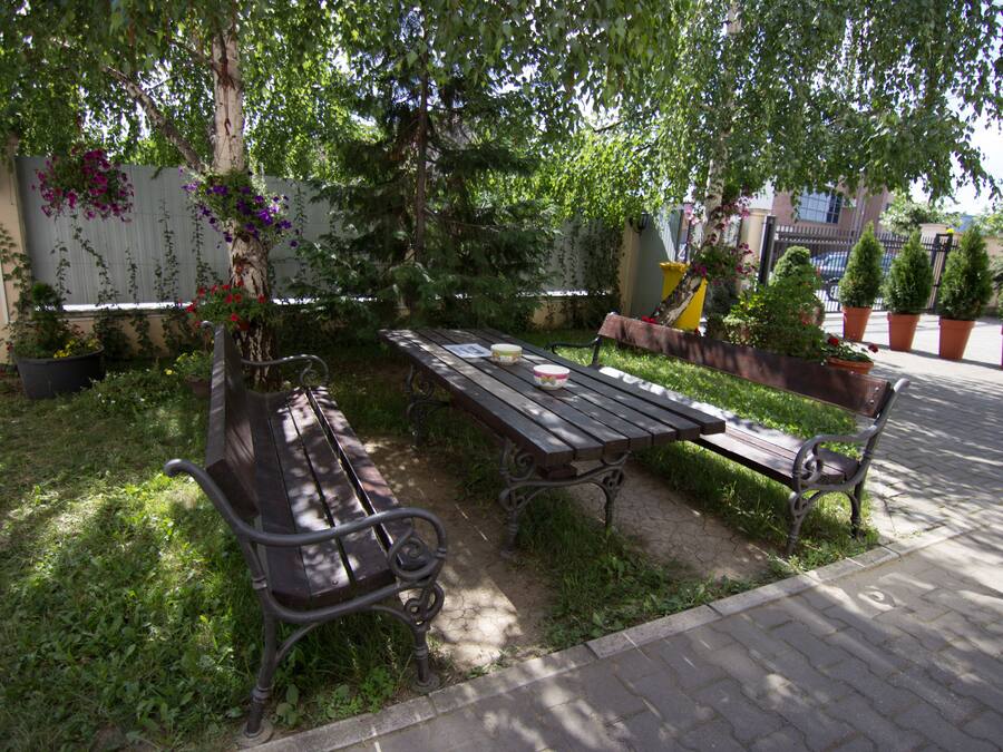 An outdoor seating area with a wooden table and benches, surrounded by potted plants and a tree.