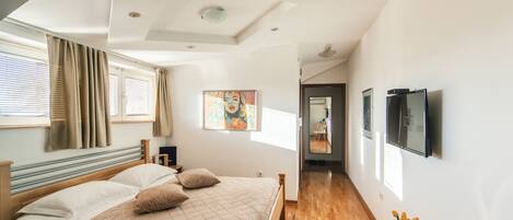 A modern bedroom with a large bed, wooden headboard, and a small white side table with a vase of flowers.