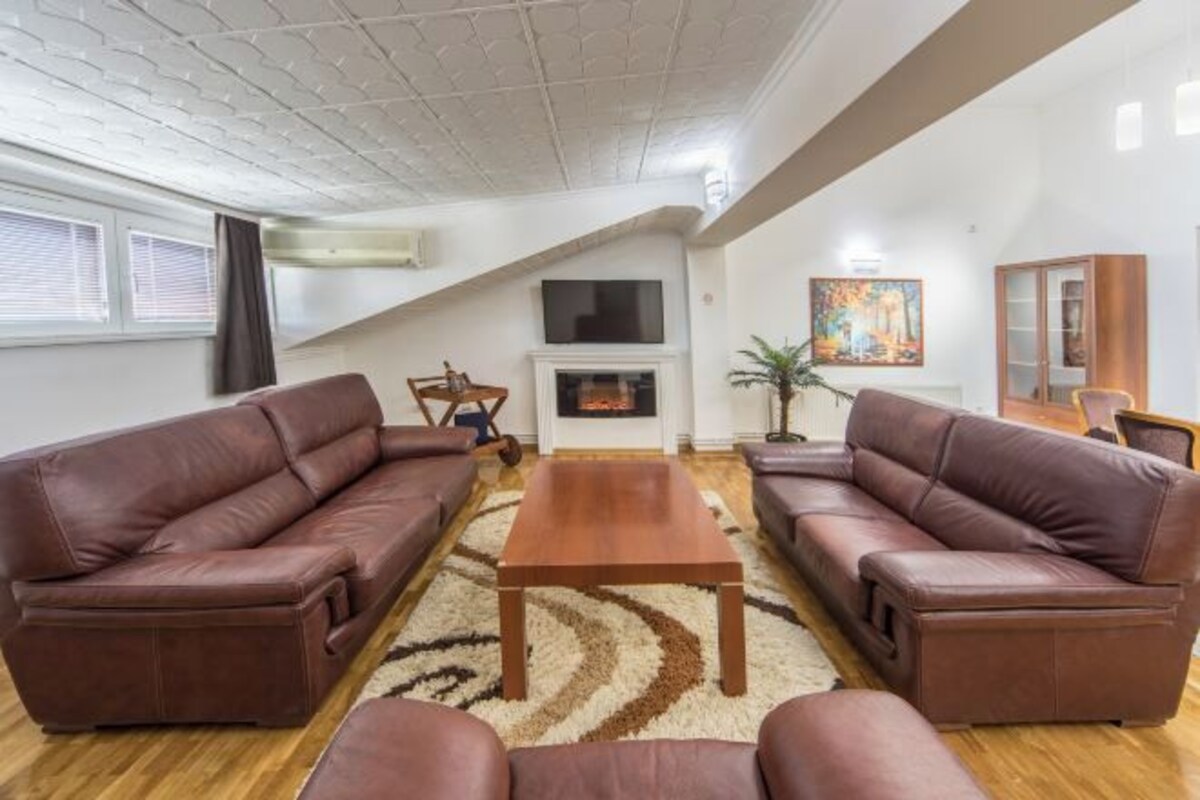 Un salón con dos sofás de cuero marrón, una mesa de centro de madera, un televisor de pantalla plana sobre la chimenea y un cuadro en la pared.