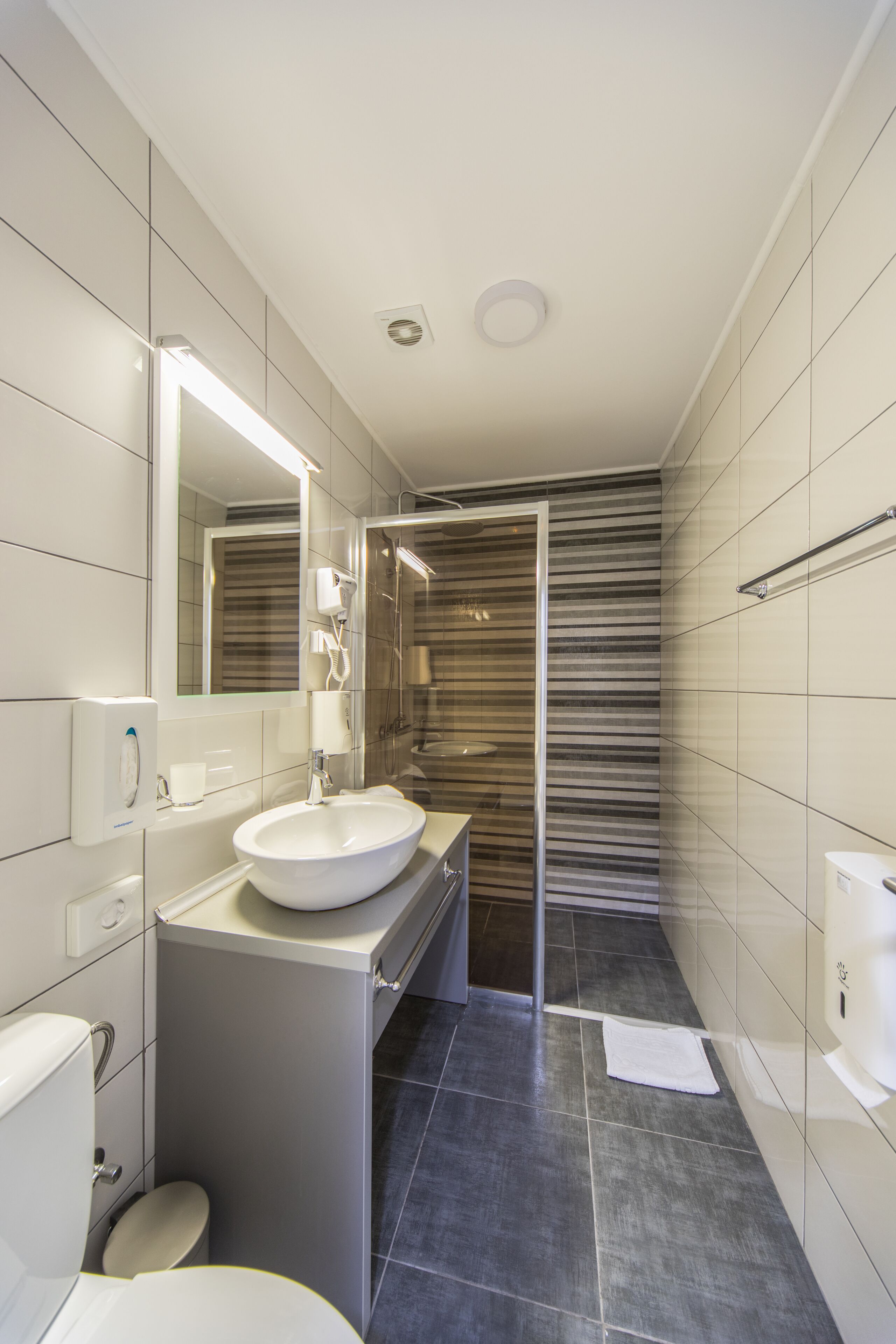 Un baño moderno con un espejo grande, un lavabo, un inodoro y una zona de ducha.