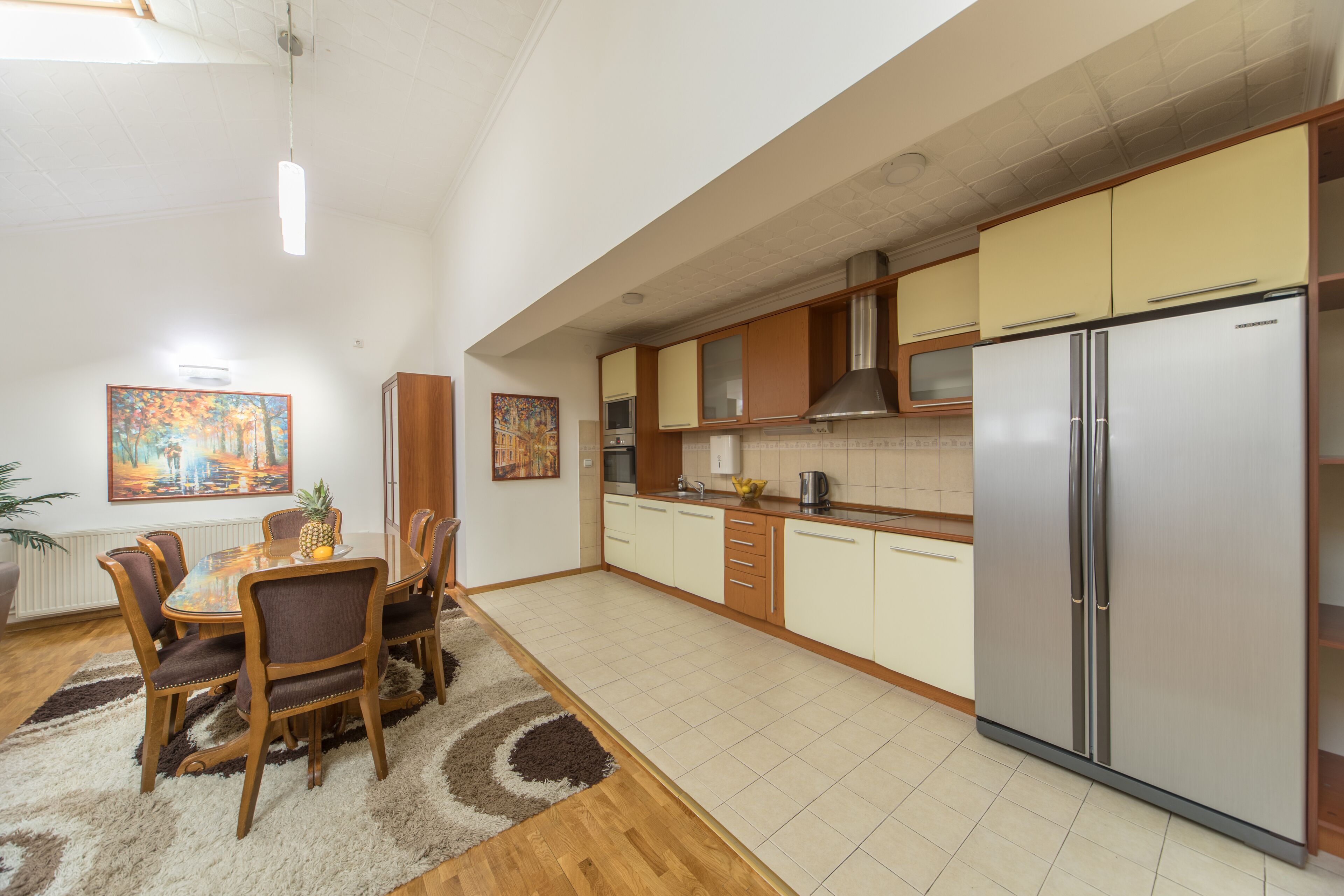 Una cocina moderna con armarios de madera, un refrigerador de acero inoxidable y un comedor con una mesa redonda y sillas.