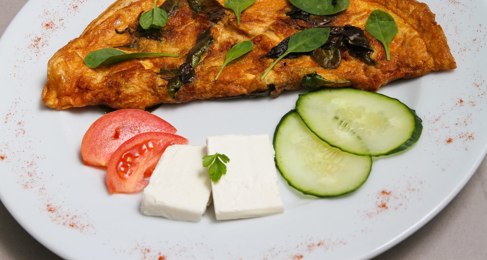 A plate with a grilled dish, tomato slices, cucumber slices, and a block of cheese.