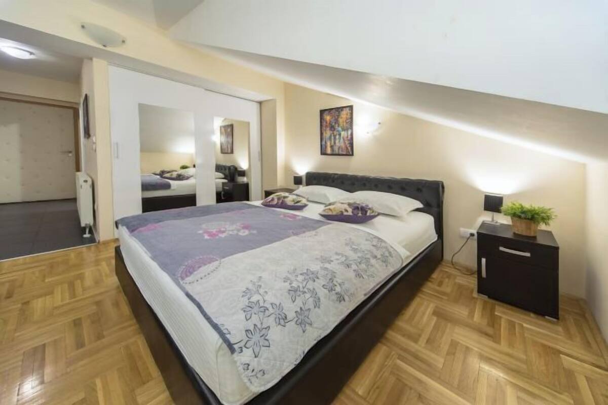 Quarto com cama, mesas de cabeceira, um espelho e um quadro na parede.