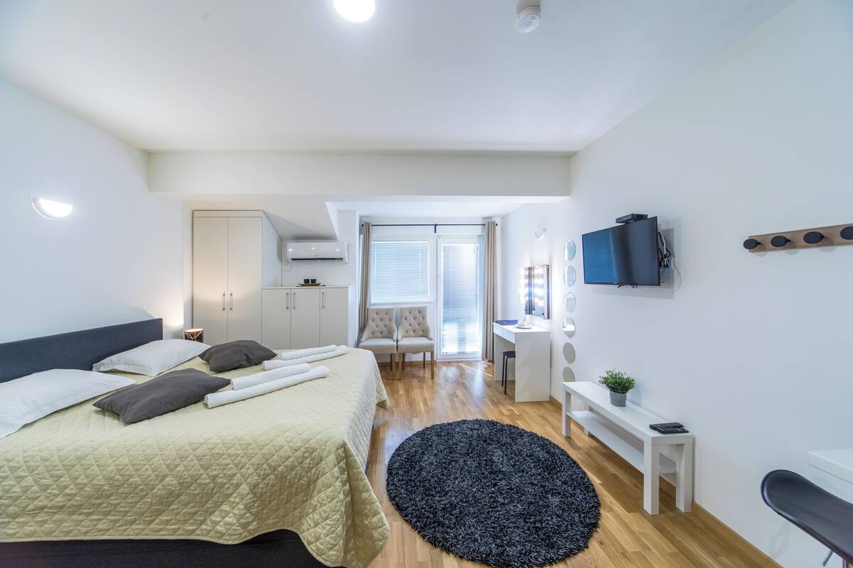 Quarto moderno com cama, mesa de cabeceira e televisão fixada na parede.