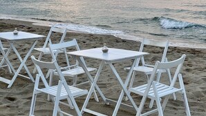 A beach with white tables and chairs arranged for dining, overlooking the sea.