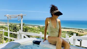 Una persona sentada en un jacuzzi con vistas panorámicas del océano y del paisaje.