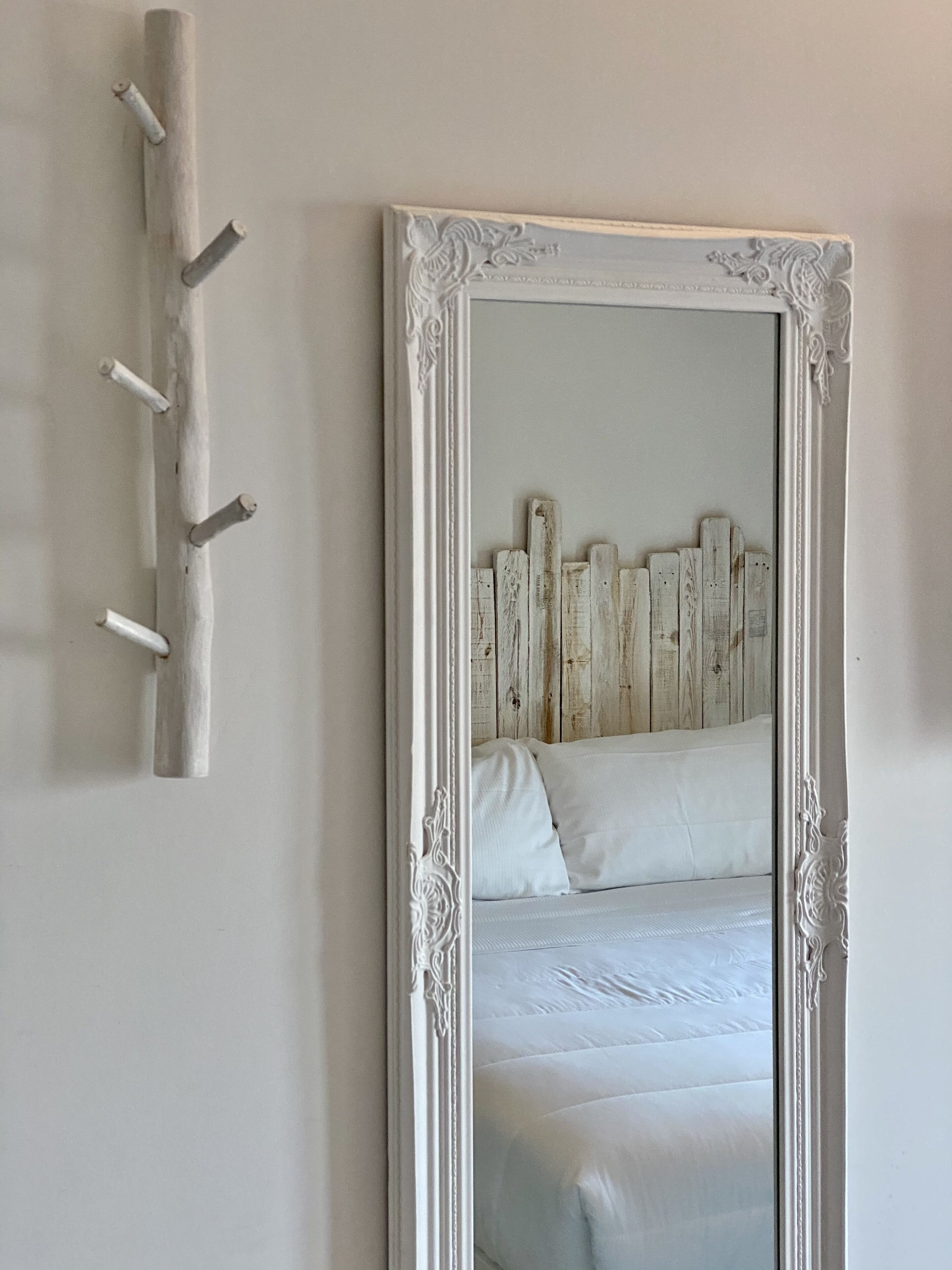 A bedroom with a large ornate mirror, a wooden headboard, and a wall-mounted light fixture.