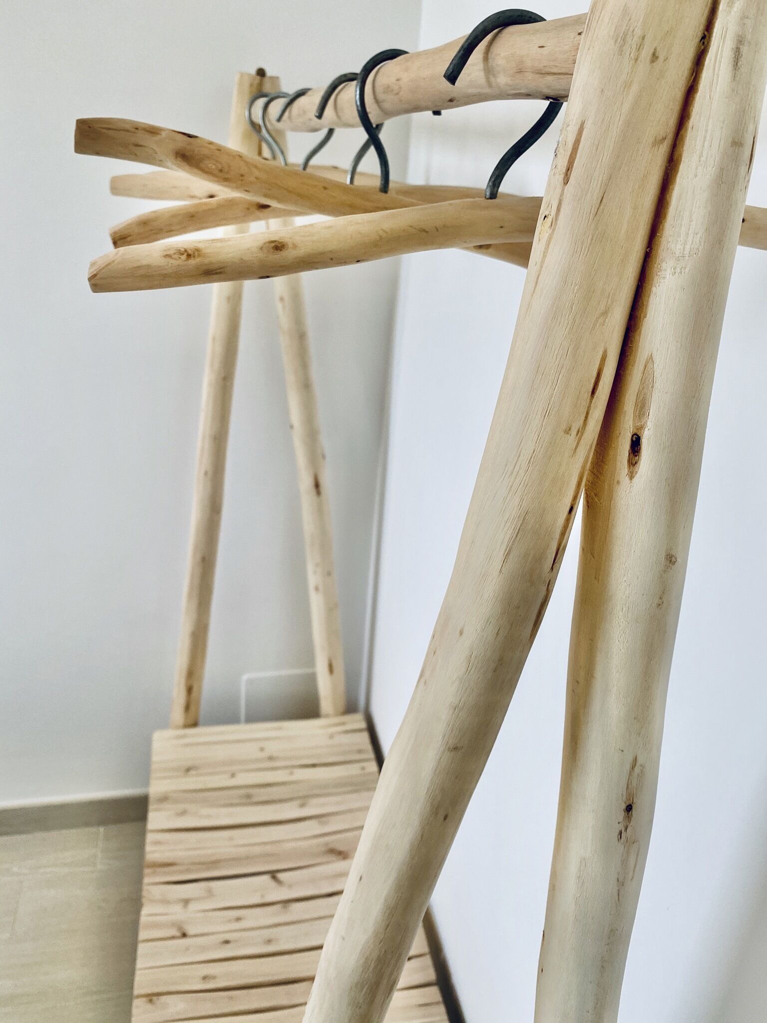 Eine Holzkonstruktion mit Metallhaken, vermutlich ein Wäscheständer, in einem Raum mit Holzboden.