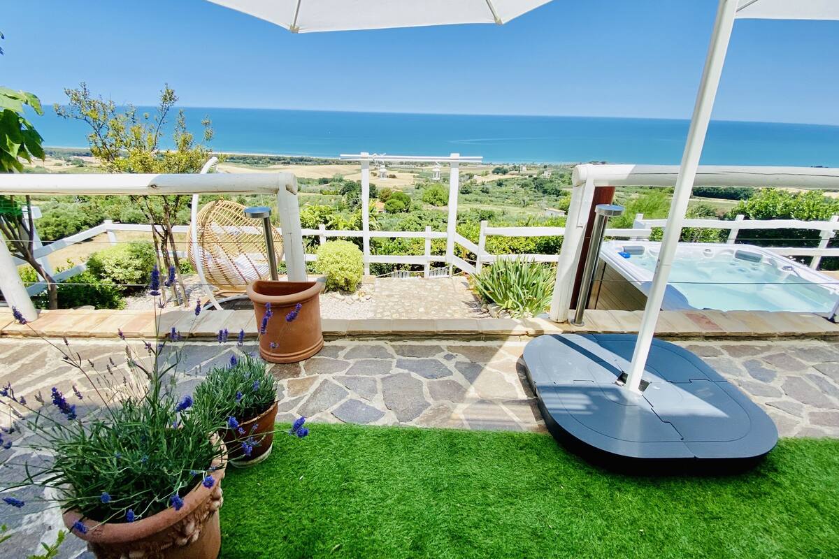 A patio with a view of the sea, a hot tub, and potted lavender plants.