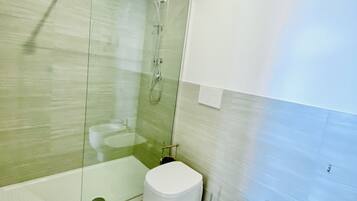 A modern bathroom with a glass-enclosed shower, a toilet, and a bidet.