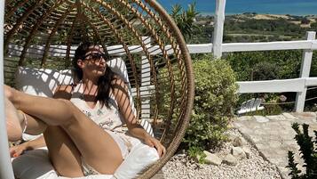 A person relaxing in a wicker swing chair overlooking a scenic landscape with a view of the sea and hills.