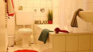 A bathroom with a toilet, a bathtub, a towel rack, a potted plant, and a sign that says "RELAX". - Eine schöne Wohnung in Kupferdreh (Essen)