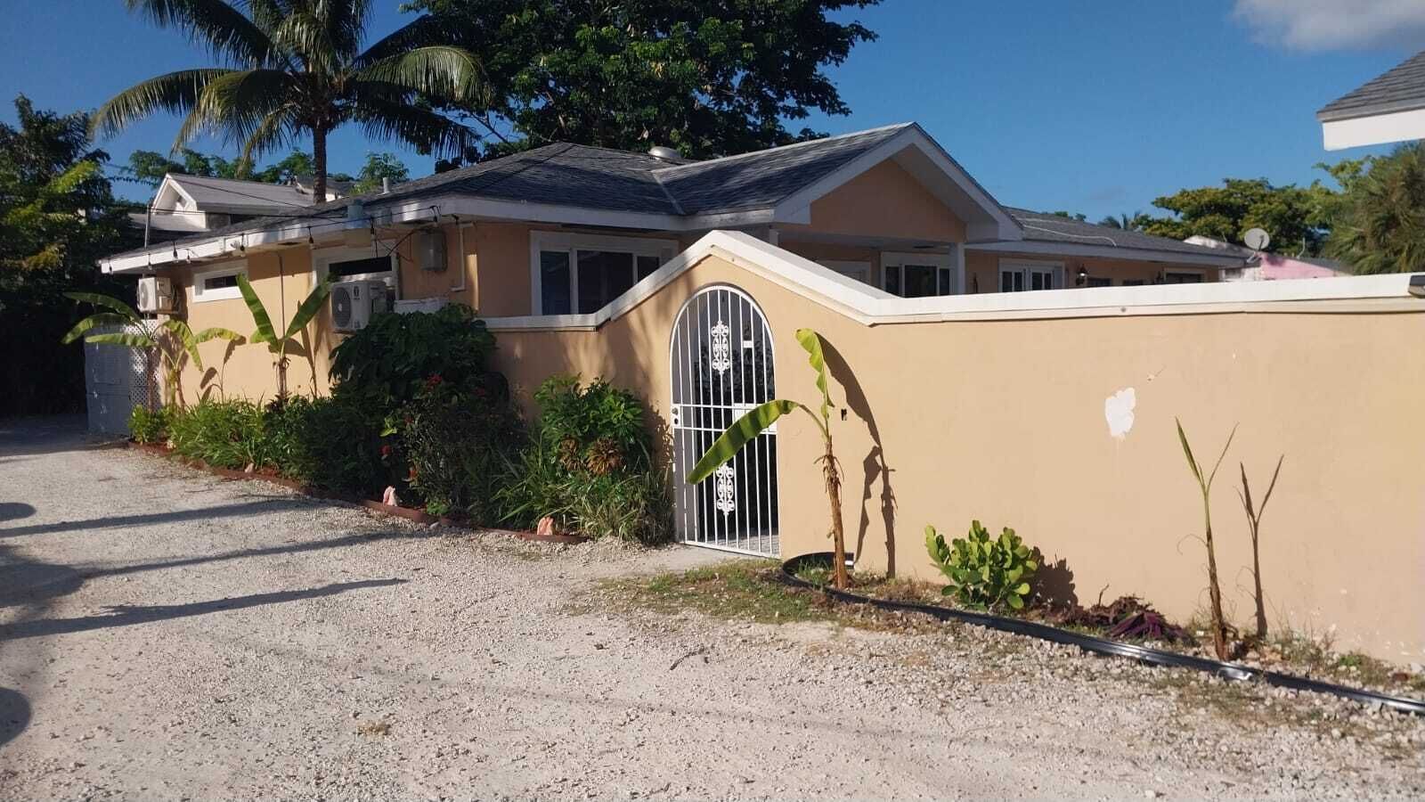 Una casa residencial con entrada de grava, un acceso con portón y un pequeño jardín con diversas plantas.