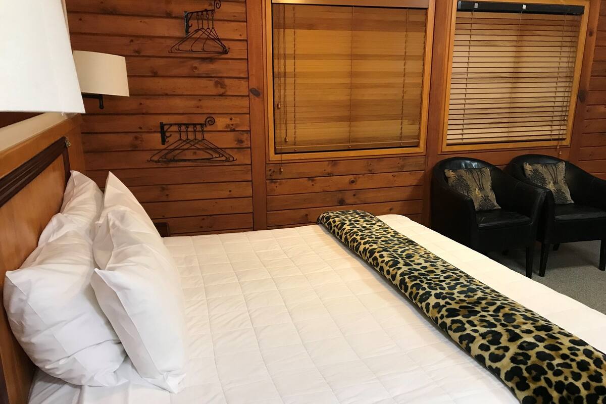 Une pièce en bois avec un lit, deux chaises et une fenêtre équipée de stores.