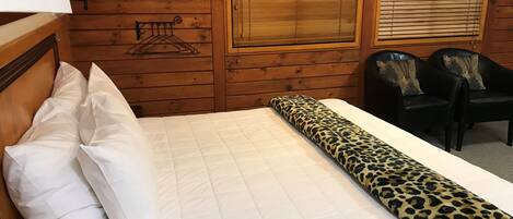 Una habitación de madera con una cama, dos sillas y una ventana con persianas.
