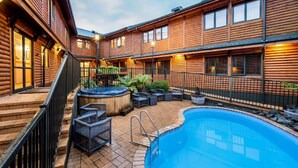 Un bâtiment de style chalet en rondins de bois, doté d’une piscine, d’un espace salon extérieur et d’un jacuzzi.