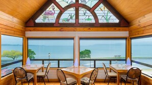 Un intérieur en bois avec une grande table et des chaises, de grandes fenêtres donnant sur la mer et un vitrail au-dessus.