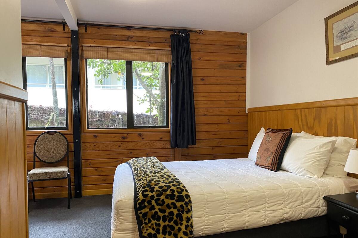 Une chambre à coucher avec un lit, une chaise, une fenêtre et un mur en bois.