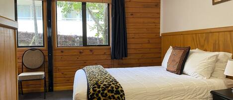 A bedroom with a bed, a chair, a window, and a wooden wall.