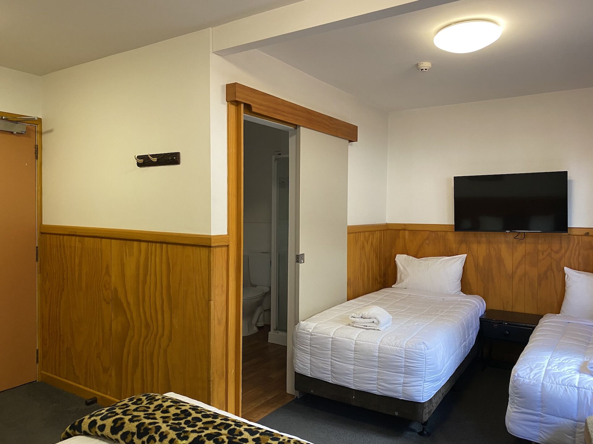 A hotel room with two beds, a television mounted on the wall, and a wooden wardrobe.