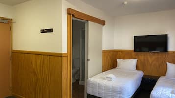 Una camera d'albergo con due letti, una televisione a muro e un armadio in legno.