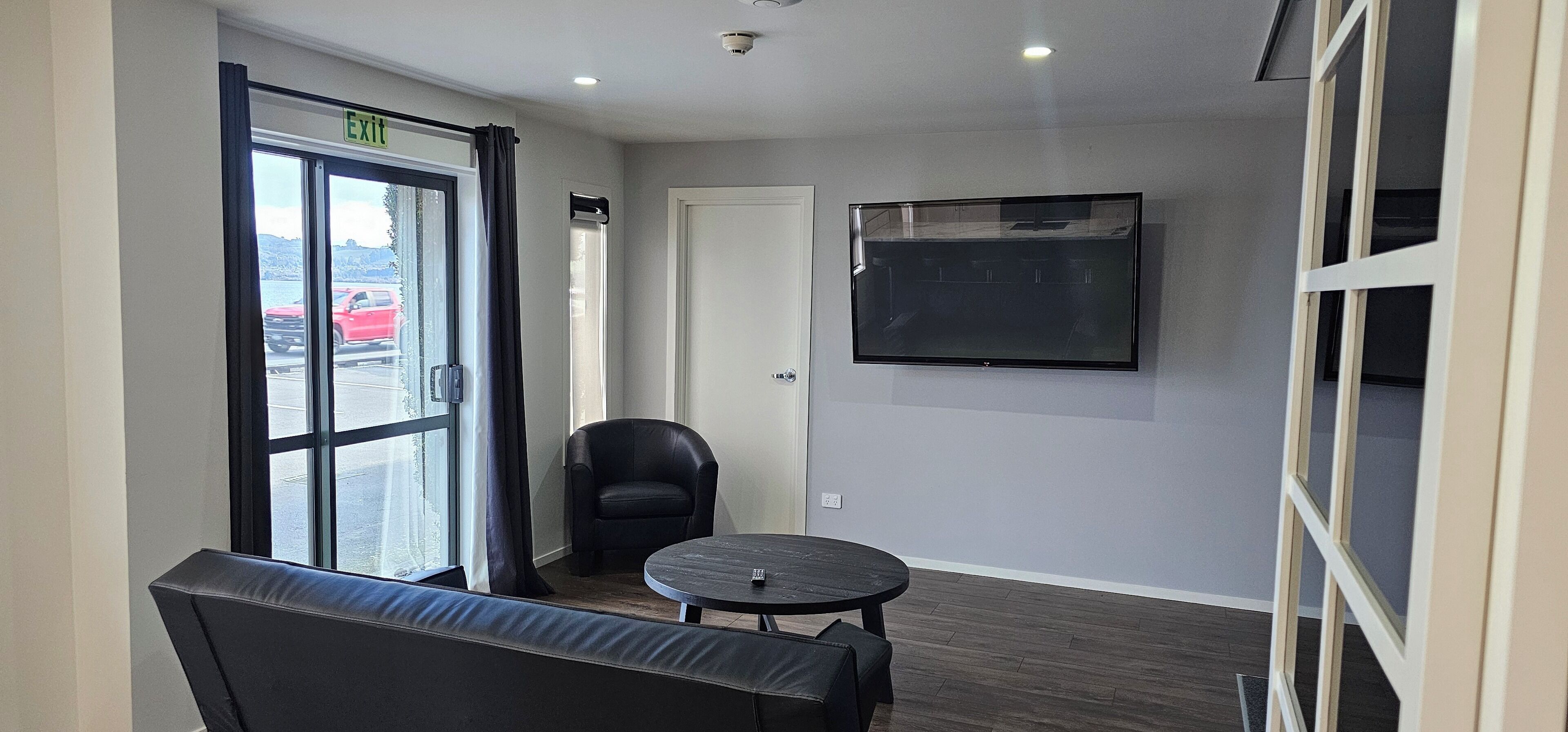 A modern room with a large window, a black leather chair, a round table, and a mounted TV.