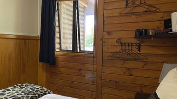 Quarto estilo cabana de madeira, com uma cama, janela com persianas e dois porta-casacos fixados na parede.