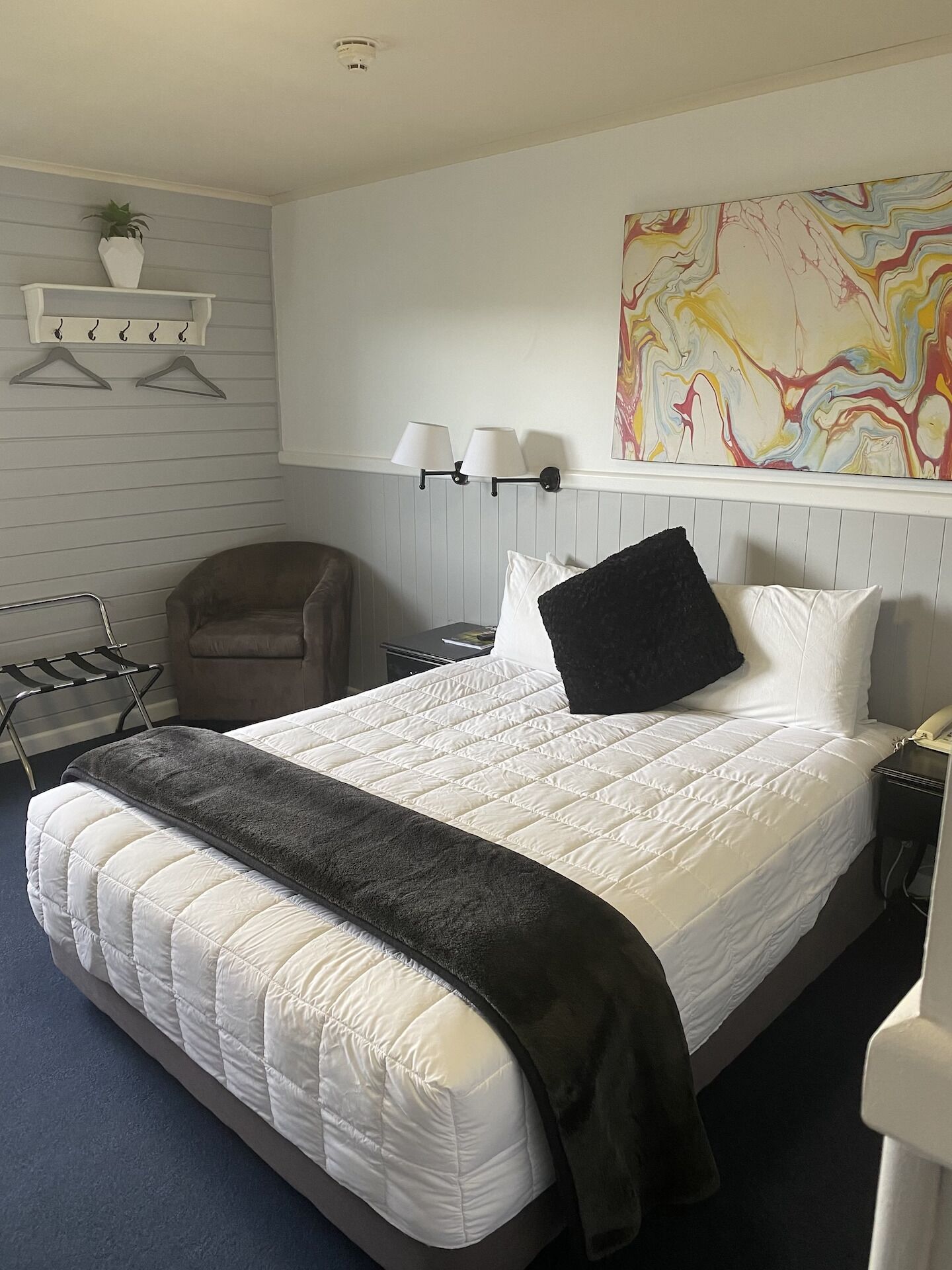 Een netjes ingerichte hotelkamer met een groot bed, een stoel, een nachtkastje, een lamp en een wandplank met een plant.