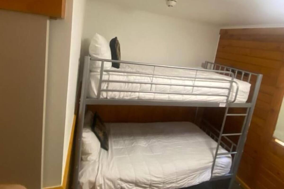 Une chambre avec un lit superposé, une tête de lit en bois, un mur blanc et un luminaire au plafond.