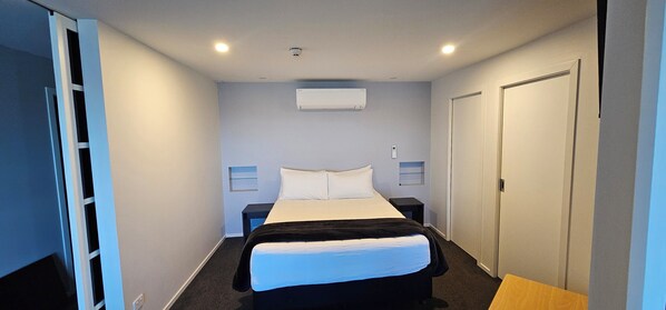 A hotel room with a bed, bedside tables, a wardrobe, and an air conditioning unit.