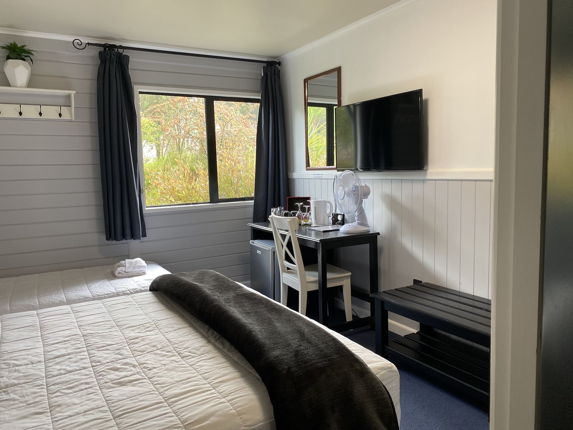 A hotel room with a bed, a desk with a chair, a TV, and a window with curtains.