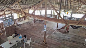 An open-air wooden structure with a thatched roof, featuring a dining area with tables and chairs, a hammock, and a view of the sea. -  San Blas Paradise Private Cabins on Shipwreck Island - meals included (Ailigandi)