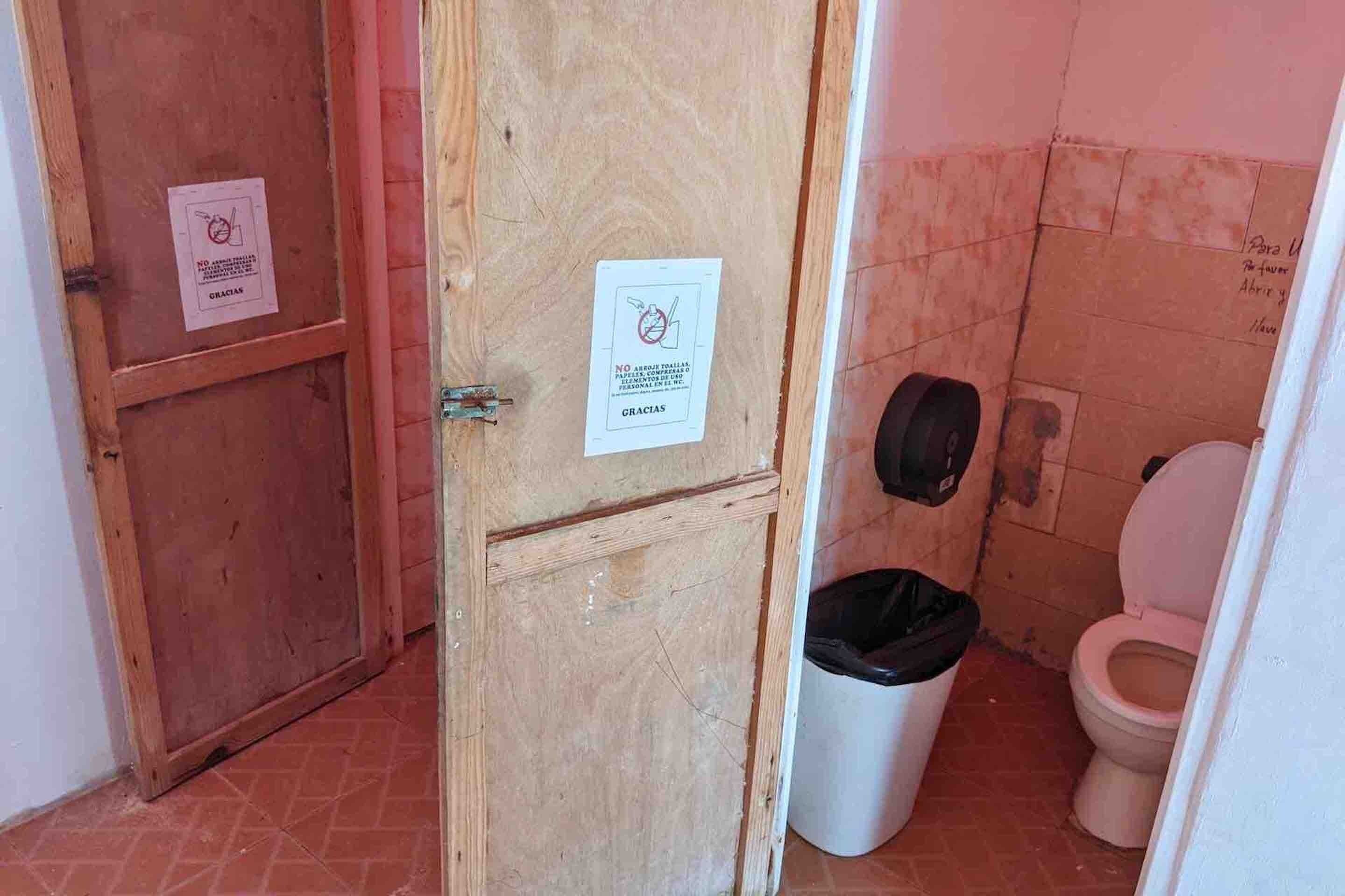 Un baño con puerta de madera, un bote de basura blanco y un inodoro.