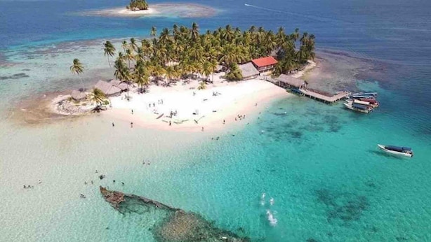 An aerial view of a tropical island with a beach, palm trees, and a dock with boats. -  San Blas Paradise Private Cabins on Shipwreck Island - meals included (Ailigandi)