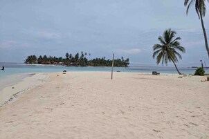 A beach with a volleyball net, palm trees, and a distant island with buildings.