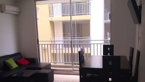 A living room with a sofa, a dining table, and chairs. There is a sliding glass door leading to a balcony with a railing. - Apartamento conjunto Entre Sierras (Valledupar)