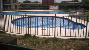 A swimming pool with a checkered pattern, surrounded by a metal fence, and a building in the background. - Apartamento conjunto Entre Sierras (Valledupar)