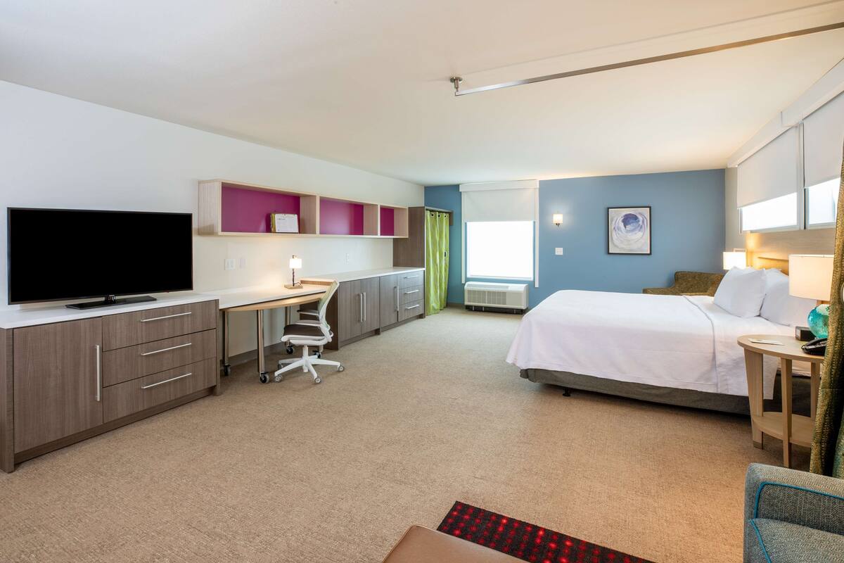 Habitación de hotel con cama, escritorio, televisión y ventana con cortinas.