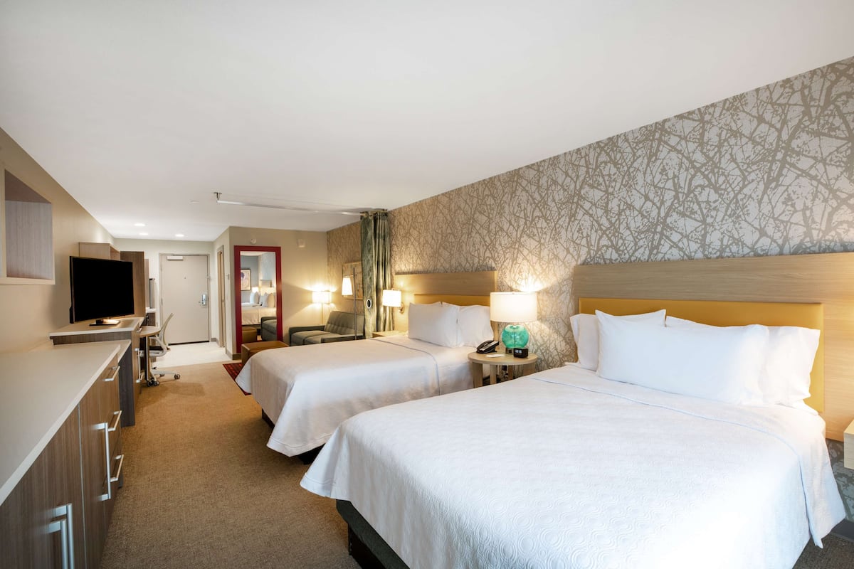 Habitación de hotel con dos camas, televisión, escritorio y baño.