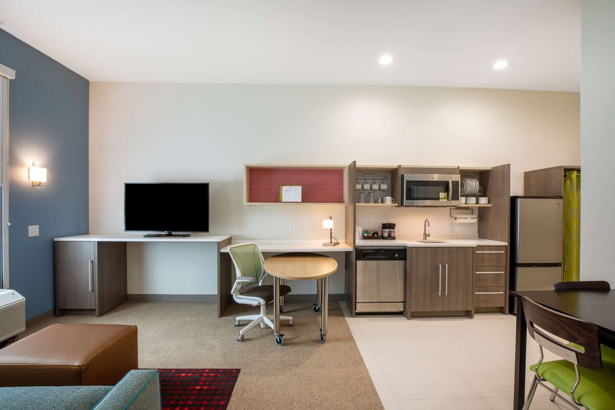 Una cocina moderna con una televisión de pantalla plana, un comedor con mesa y sillas, y una kitchenette equipada con microondas y refrigerador.