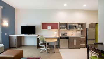 Una cocina moderna con una televisión de pantalla plana, un comedor con mesa y sillas, y una kitchenette equipada con microondas y refrigerador.
